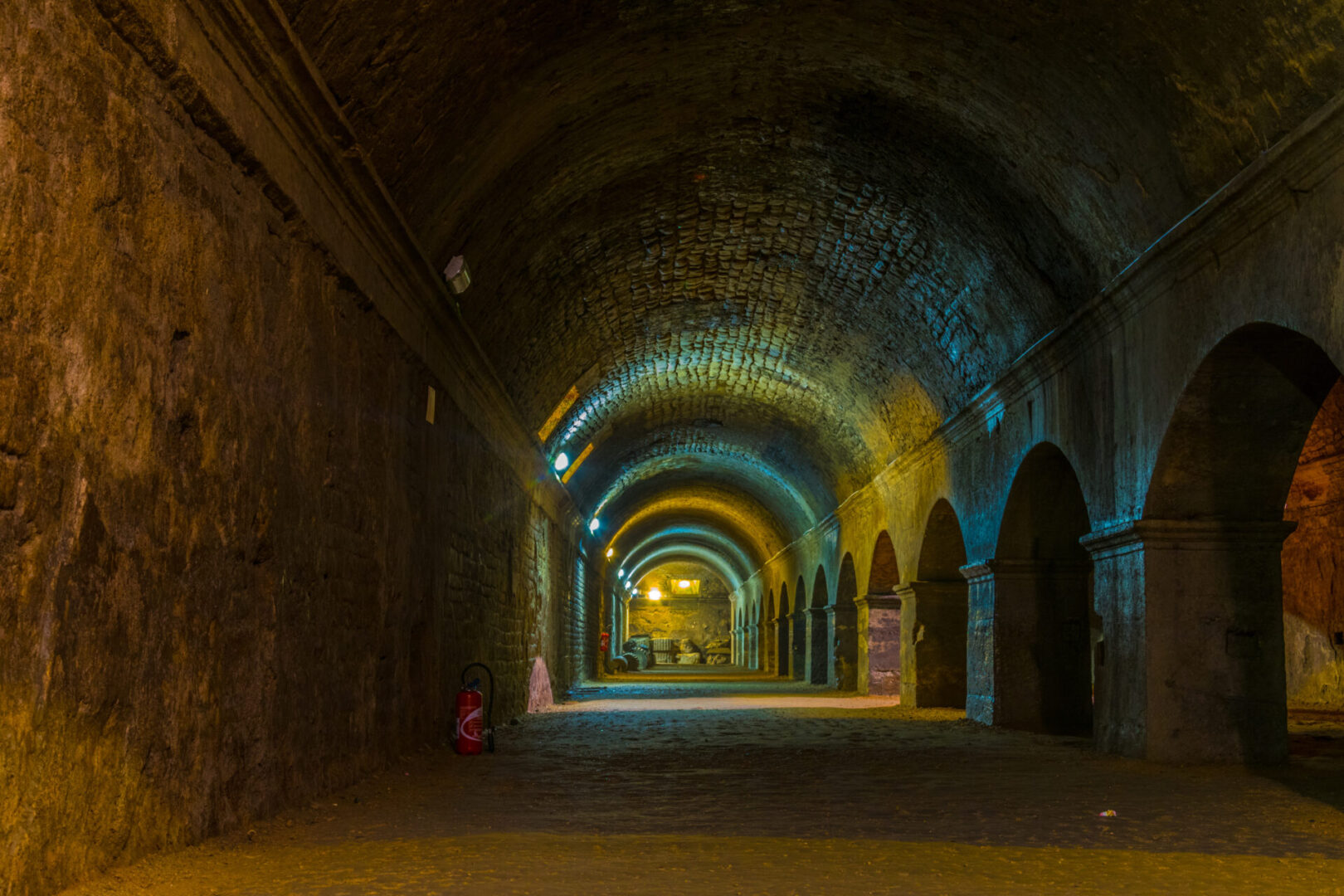 Dimly lit arched corridor with warm lighting and stone walls.